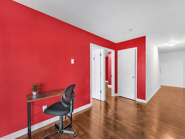 Open common area with hardwood floors, bold accent wall, and a small work desk near multiple interior doorways.
