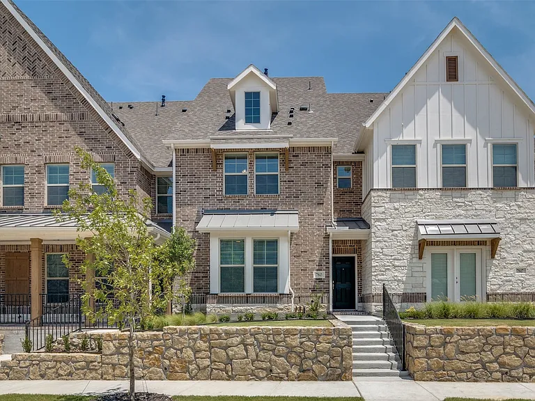 Contemporary townhome facade featuring a blend of brick and stone masonry, board-and-batten siding, multiple gables, and a prominent front entrance with a dark door
