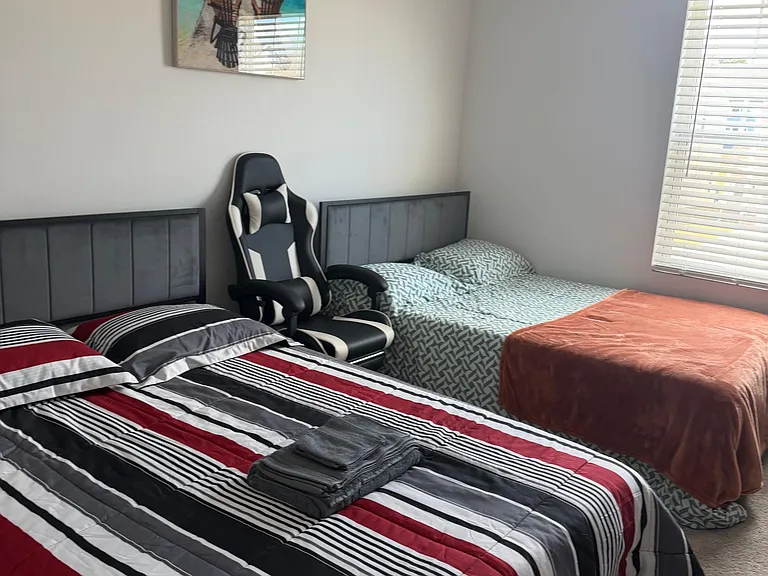 Furnished bedroom with two beds, comfortable seating, and a window with blinds for natural light and privacy.