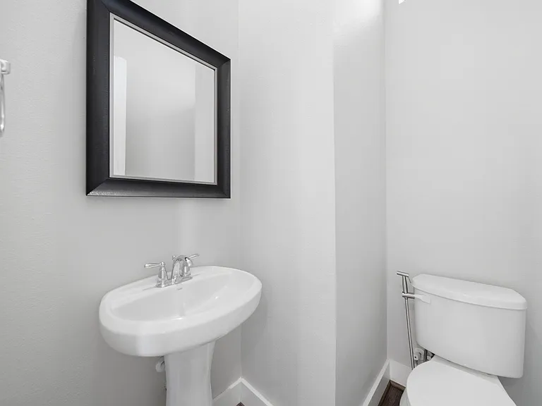 Modern, well-appointed half-bath featuring a sleek pedestal sink, framed mirror, and updated toilet. Clean, minimalist design with neutral tones creates a bright, polished space that feels fresh and inviting_perfect for guests and everyday convenience.