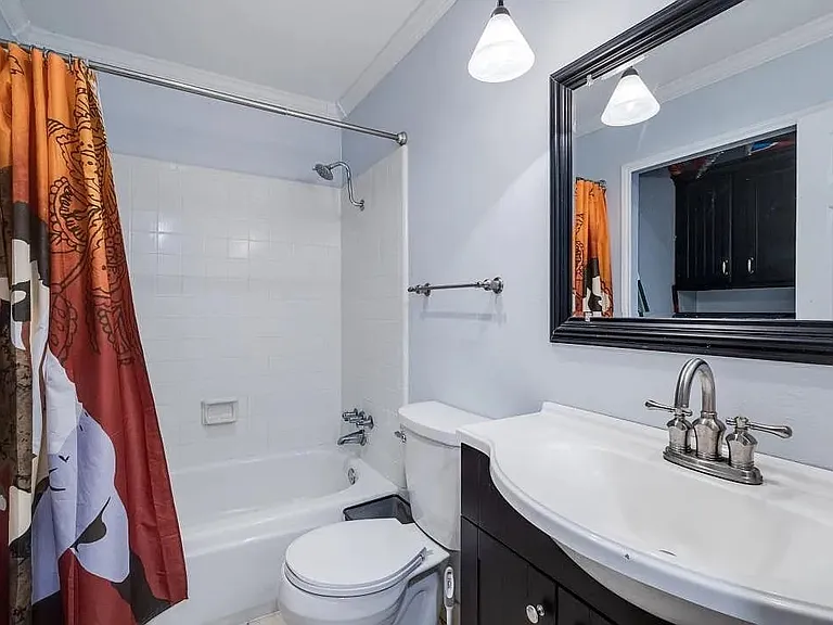 Bathroom featuring a white bathtub and shower with white tile surround, a dark wood-finish vanity with an integrated white sink, a chrome two-handle faucet, and an ornate black framed mirror
