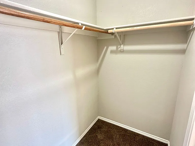 Walk-in closet with wraparound hanging rods and open floor space for storage bins and organizers.