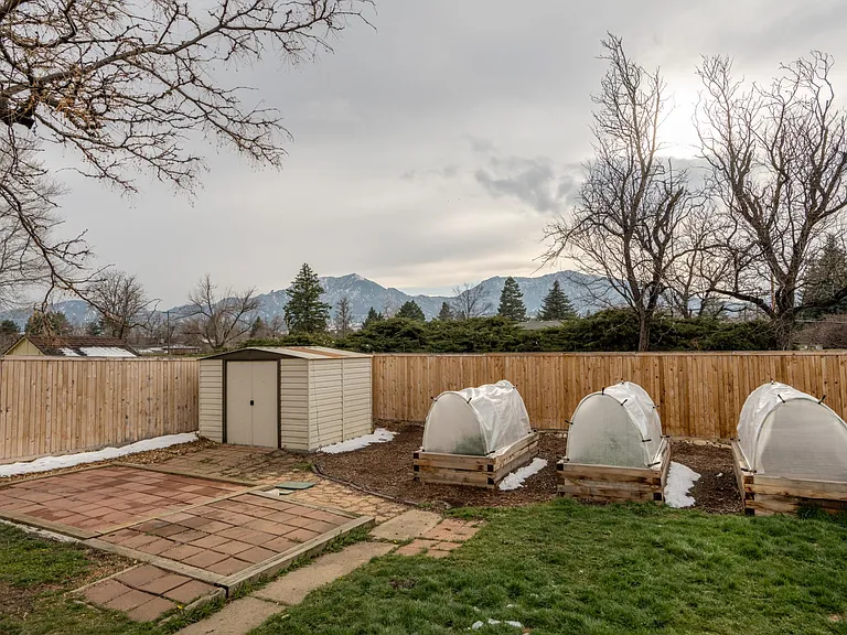View from the house towards Bear Peak and the Flatirons. In the foreground is a paved pad, the raised garden beds, and a garden shed.