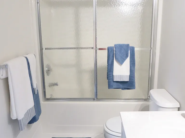 Primary bath with tub and glass shower doors and white cabinetry.