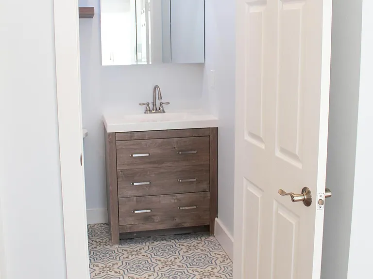 View of bathroom. Mediterranean-style tile brings the neutral colors together between the light blue walls and white washed oak vanity with marble sink. Storage in vanity dresser drawers and large mirrored medicine cabinet.