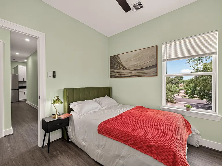 Well-appointed bedroom with a comfortable bed, bedside table, and large window offering tree-lined views.