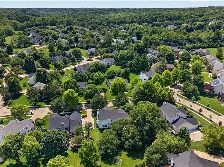 Expansive residential area with numerous houses featuring diverse architectural styles, surrounded by mature trees and verdant landscaping