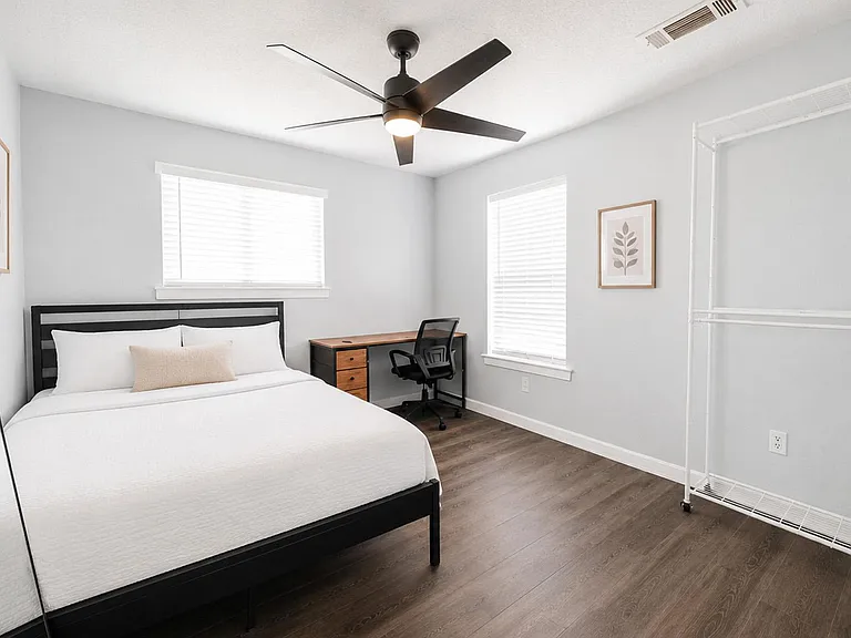 Well-sized bedroom with two windows, ceiling fan, a work desk, and ample space for storage or a clothing rack.