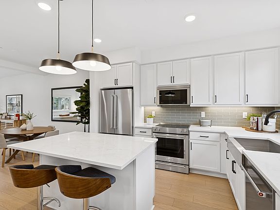 A modern, well-lit kitchen with white cabinets, stainless steel appliances, and a large central isla