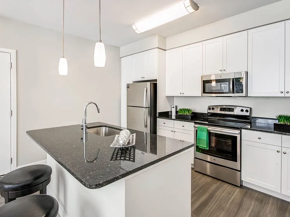 Kitchen with granite countertops, white shaker cabinetry, stainless steel appliances, kitchen island and hard surface flooring - Avalon Laurel