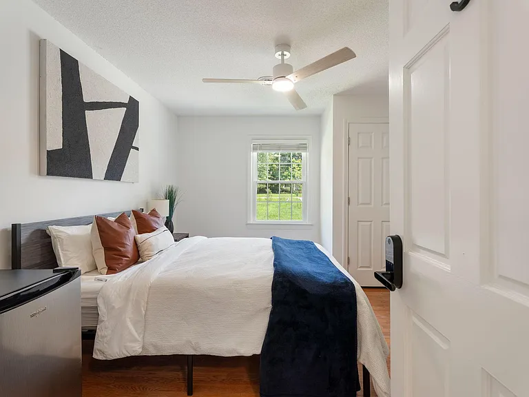 Furnished bedroom with a queen bed, ceiling fan, and window views, plus in-room mini fridge for added convenience.