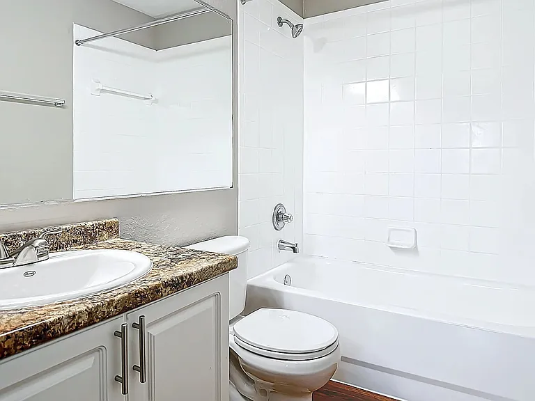 Enjoy the clean and contemporary design of this bathroom, featuring a granite-style countertop, sleek white cabinetry, and a pristine tiled shower and bathtub combo.