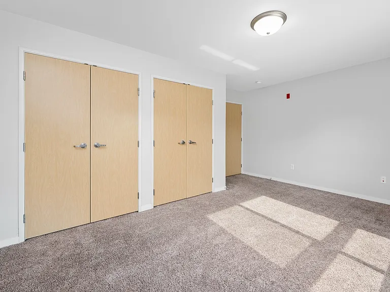 Bright, spacious empty room featuring soft beige carpeting and double wooden closet doors, illuminated by natural sunlight. Bright, spacious empty room featuring soft beige carpeting and double wooden closet doors, illuminated by natural sunlight.