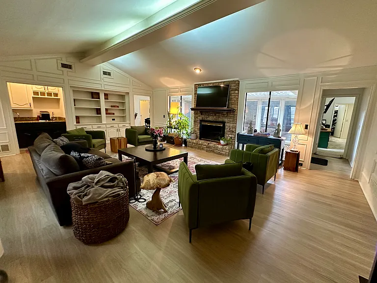 Living area featuring a brick fireplace, built in shelves, vaulted ceiling with beams, light wood-type flooring