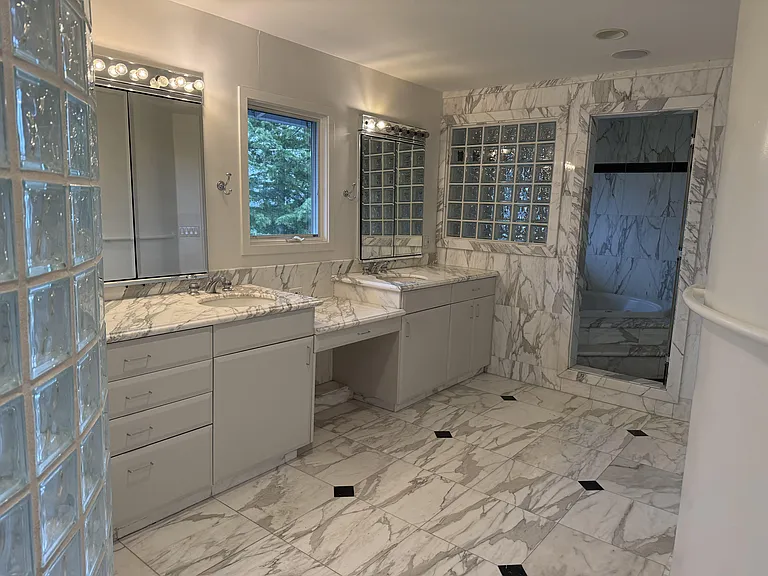 In-suite primary bathroom is tastefully appointed with glass block walls featuring dual sinks, Jacuzzi tub, multi-jet shower stall, a bidet, and a walk-in closet with built-in organized storage.