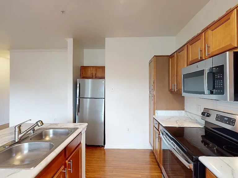 Apartment kitchen with stainless steel appliances and wood-style flooring. Quartz-style countertops (shown here) are available in select homes.