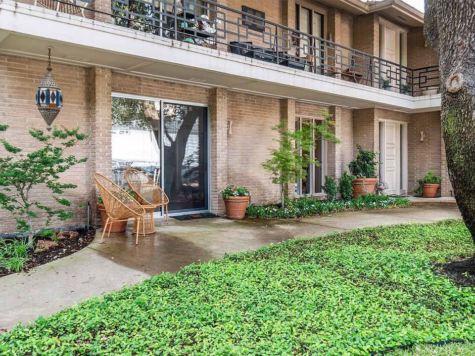 Brick exterior with a ground-level patio, mature landscaping, and an upper-level balcony featuring wrought iron railing