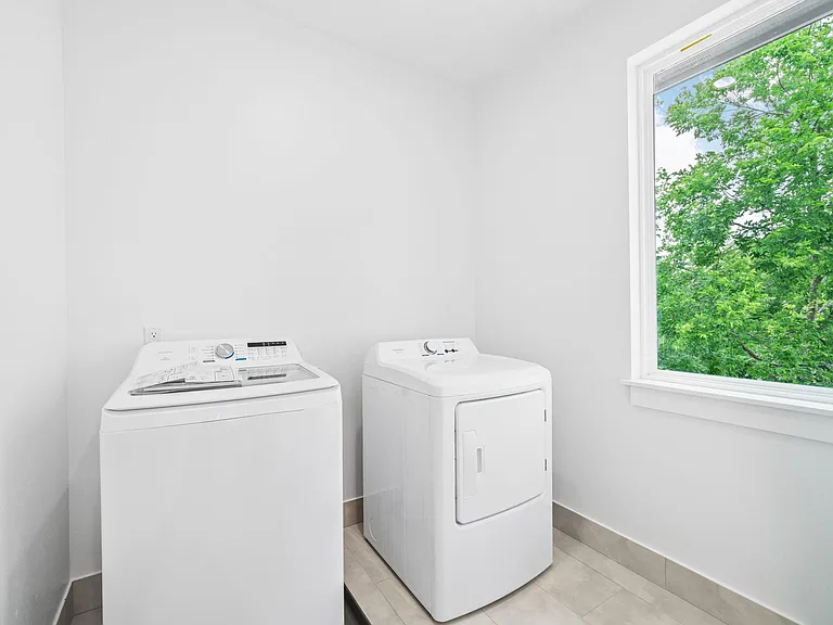 Dedicated laundry area with full-size washer and dryer, tile flooring, and a large window for ventilation and natural light.