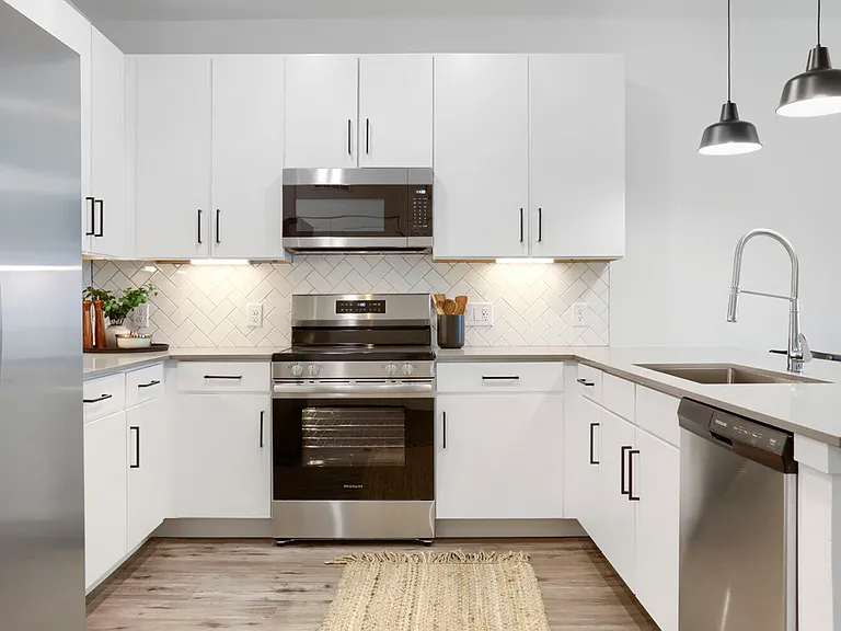 A kitchen worth cooking in. The B2 floor plan at Garrett Uptown features white shaker cabinets, stainless steel appliances, herringbone tile backsplash, and quartz countertops with under-cabinet lighting.