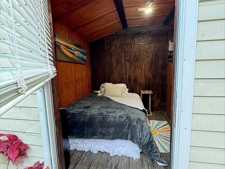 Compact sleeping nook with wood-paneled walls, vaulted ceiling, ceiling fan, and space for a bedside table.