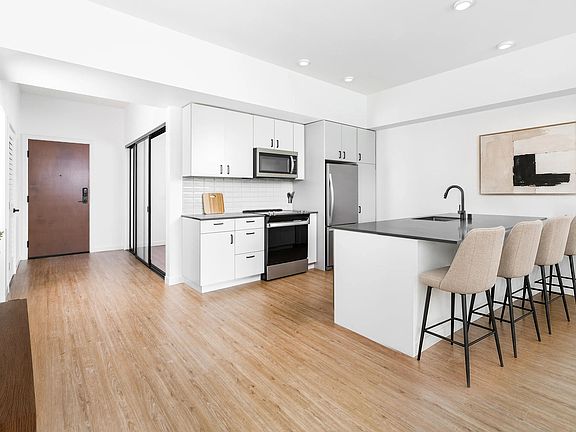 Kitchen with quartz countertops, bar seating, and streamlined cabinetry opening to a bright living area with natural light and clean finishes.