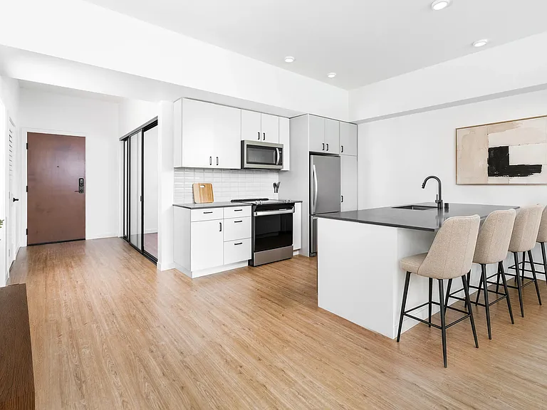 Kitchen with quartz countertops, bar seating, and streamlined cabinetry opening to a bright living area with natural light and clean finishes.
