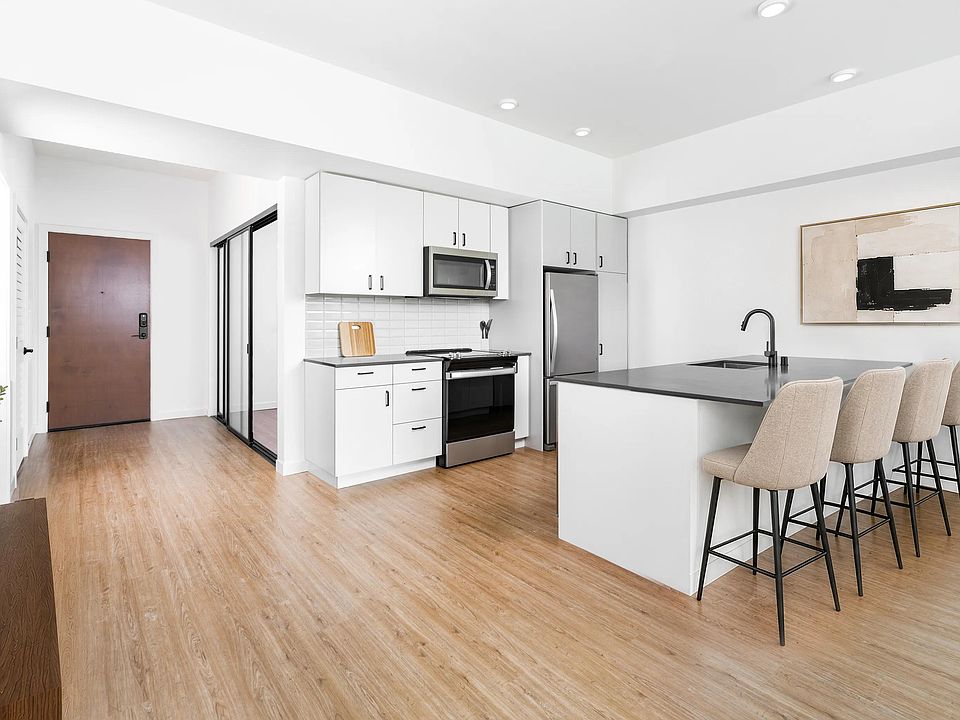 Kitchen with quartz countertops, bar seating, and streamlined cabinetry opening to a bright living area with natural light and clean finishes.
