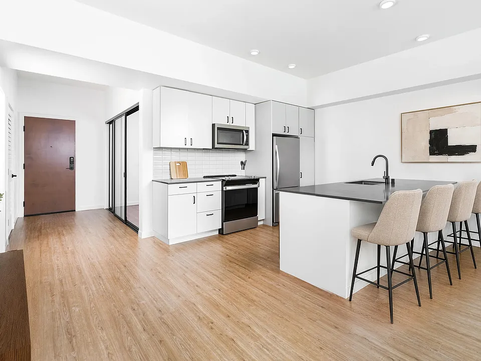Kitchen with quartz countertops, bar seating, and streamlined cabinetry opening to a bright living area with natural light and clean finishes.