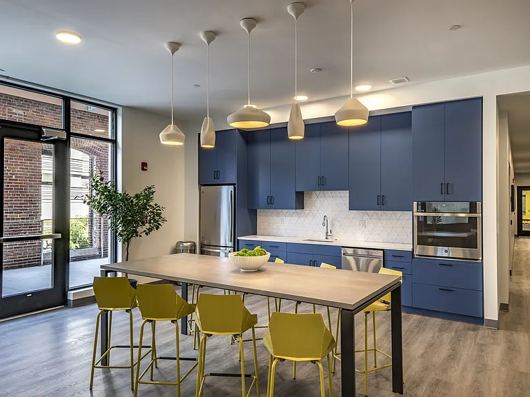 Community Kitchen With Large Table And Pendant Lighting Overhead.