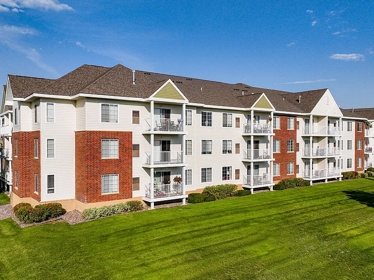 Aerial view of a modern apartment complex with spacious parking, lush greenery, and well-maintained surroundings.
