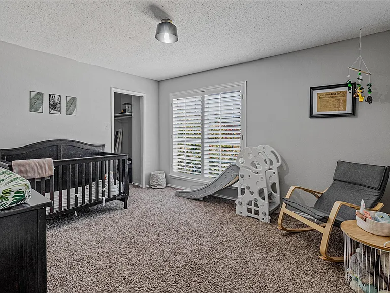 Carpeted room featuring a window with white plantation shutters, a ceiling-mounted light fixture, and a closet with an open doorway