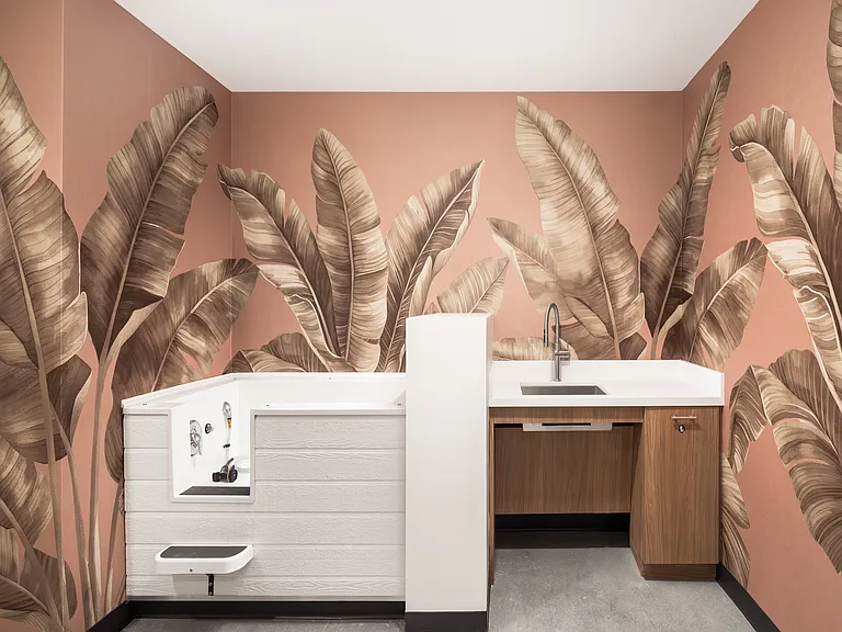 Chic laundry room with vibrant leaf-patterned wallpaper, featuring modern cabinetry and a spacious sink.