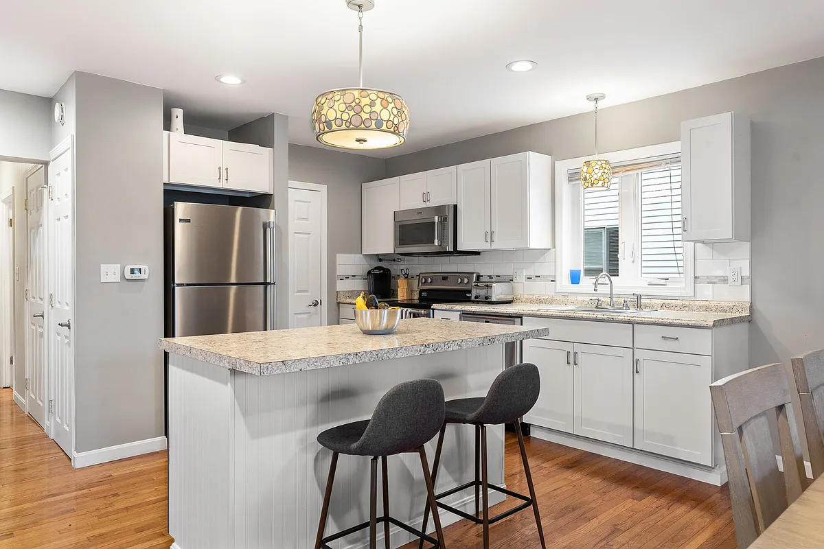 Stainless steel appliances, granite countertops, kitchen island, breakfast bar, pendant lighting, white cabinetry, hardwood flooring. - 93 High St