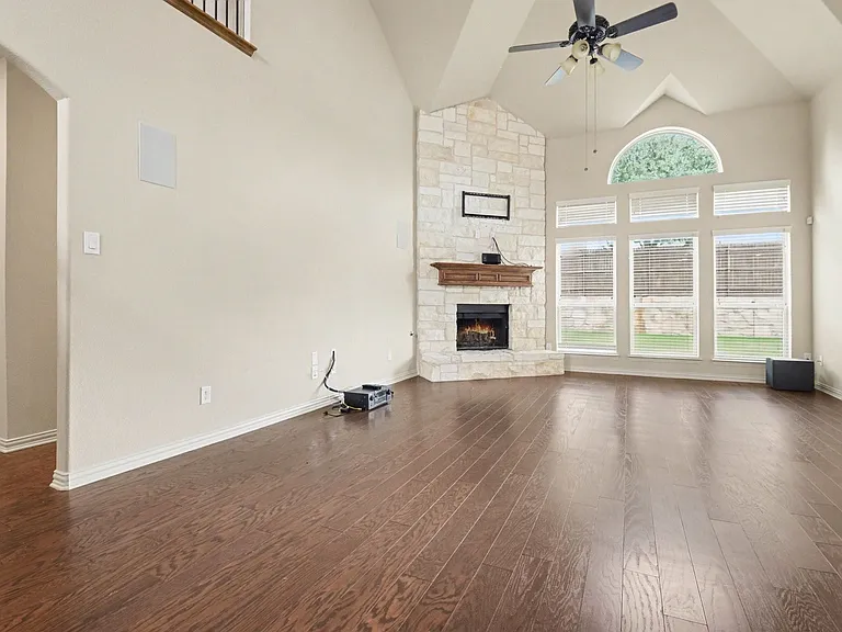 Vaulted living space featuring wood-finish flooring, a stone fireplace with a wood mantle, and a ceiling fan