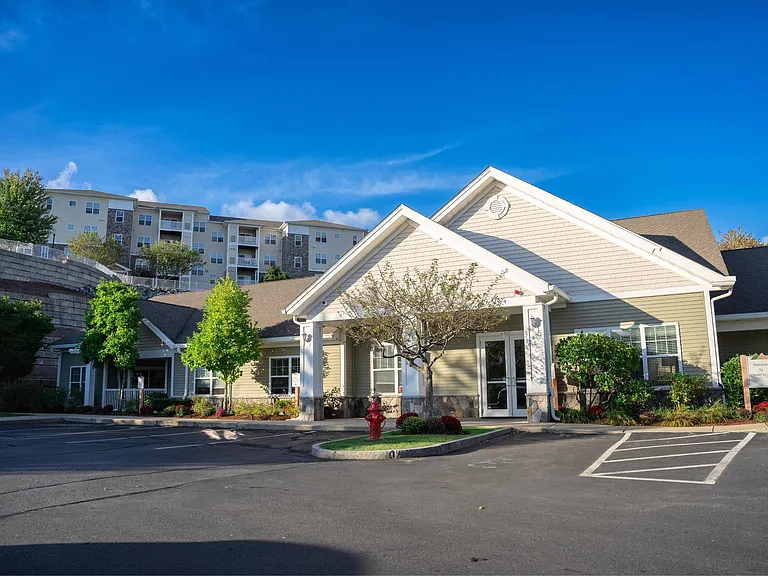 Exterior view of clubhouse and leasing office with apartment building visible on hill behind office at Summit Place apartments in Methuen, MA.