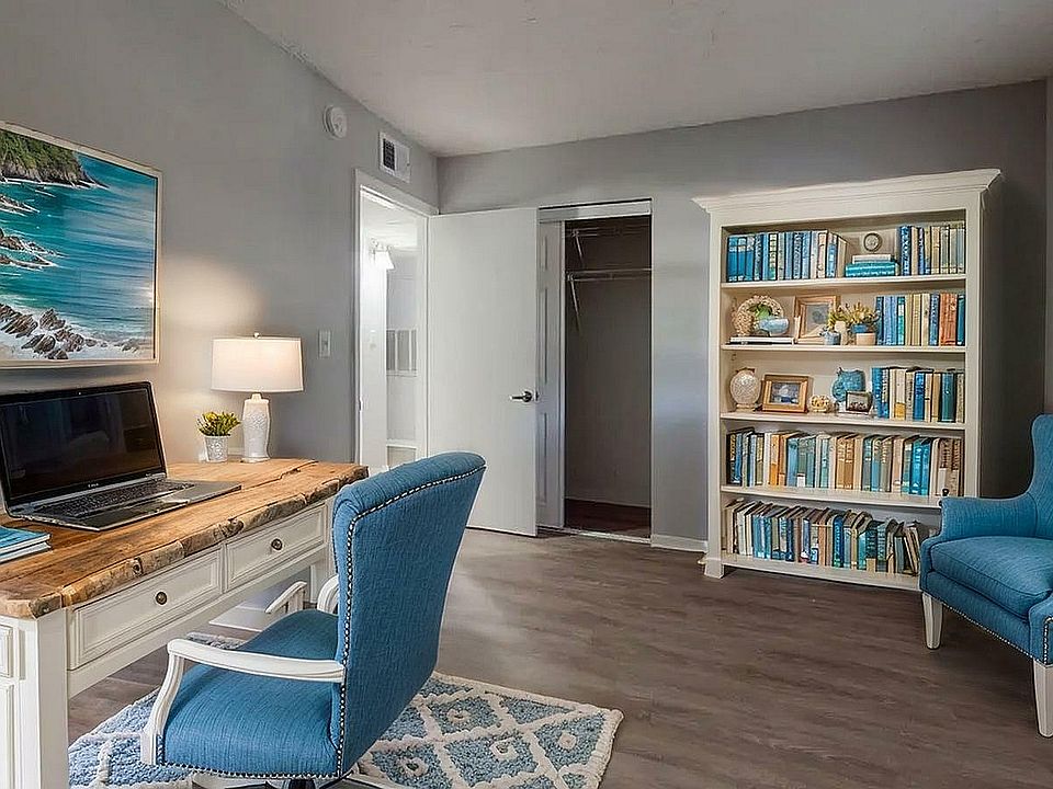 Elegant home office with a rustic wooden desk, plush blue chairs, and a spacious bookcase in a serene, calming setting.