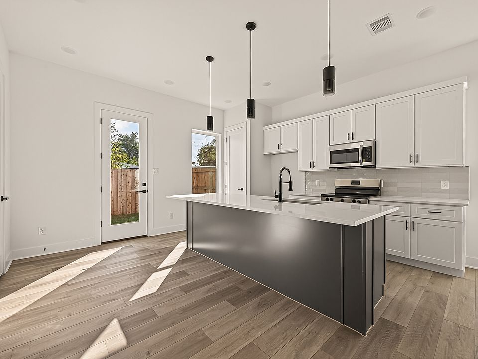 Sleek kitchen with quartz countertops, large island, and stainless steel appliances.