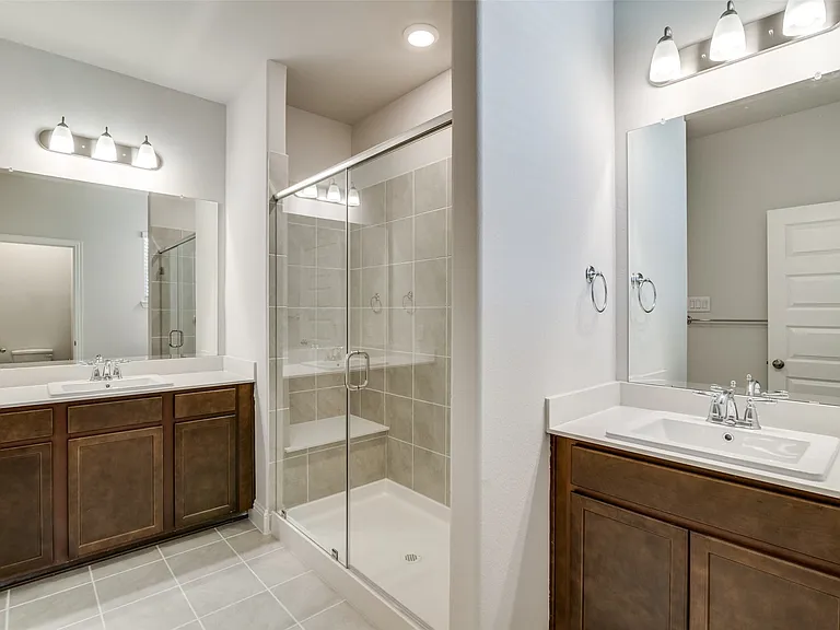 Bathroom featuring a glass-enclosed shower with integrated bench seating, dual vanities with white countertops, undermount sinks, and dark wood-finish cabinetry