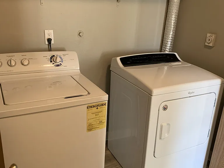 Convenient in-unit laundry area featuring a full-size washer and dryer, complete with overhead shelving for added storage and organization.