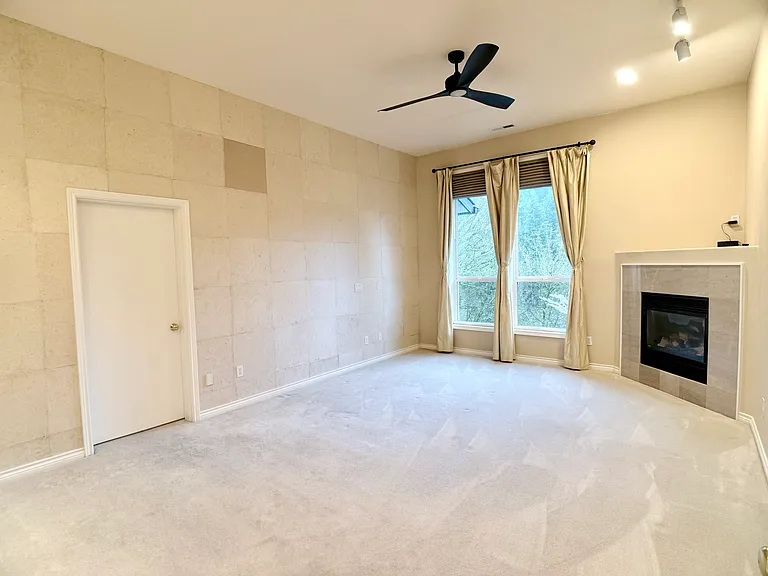 Main-level primary suite featuring a private en suite bathroom and closet, complemented by stunning views, a gas fireplace, ceiling fan, and a distinctive accent wall by a local artist.