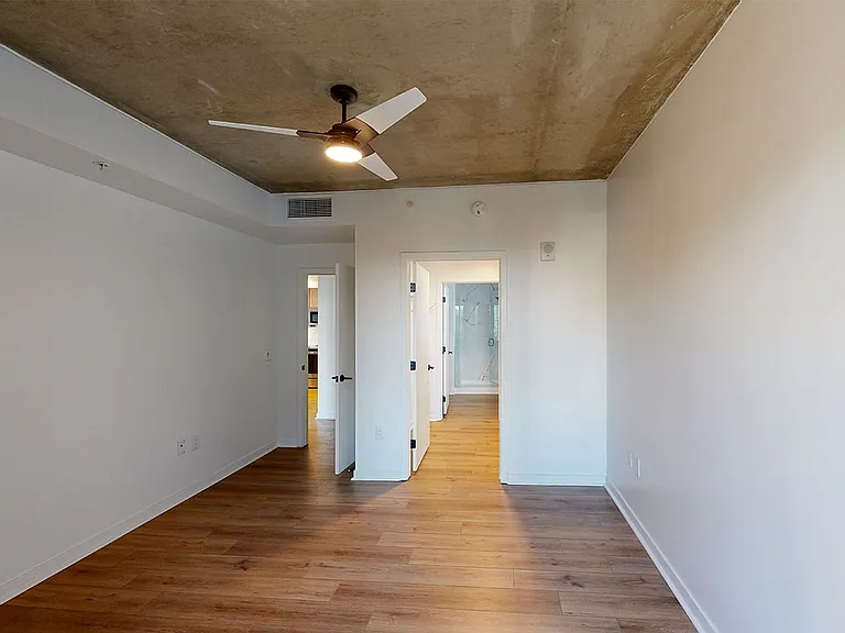Spacious apartment bedroom with large closet, attached bathroom and wood-style flooring.