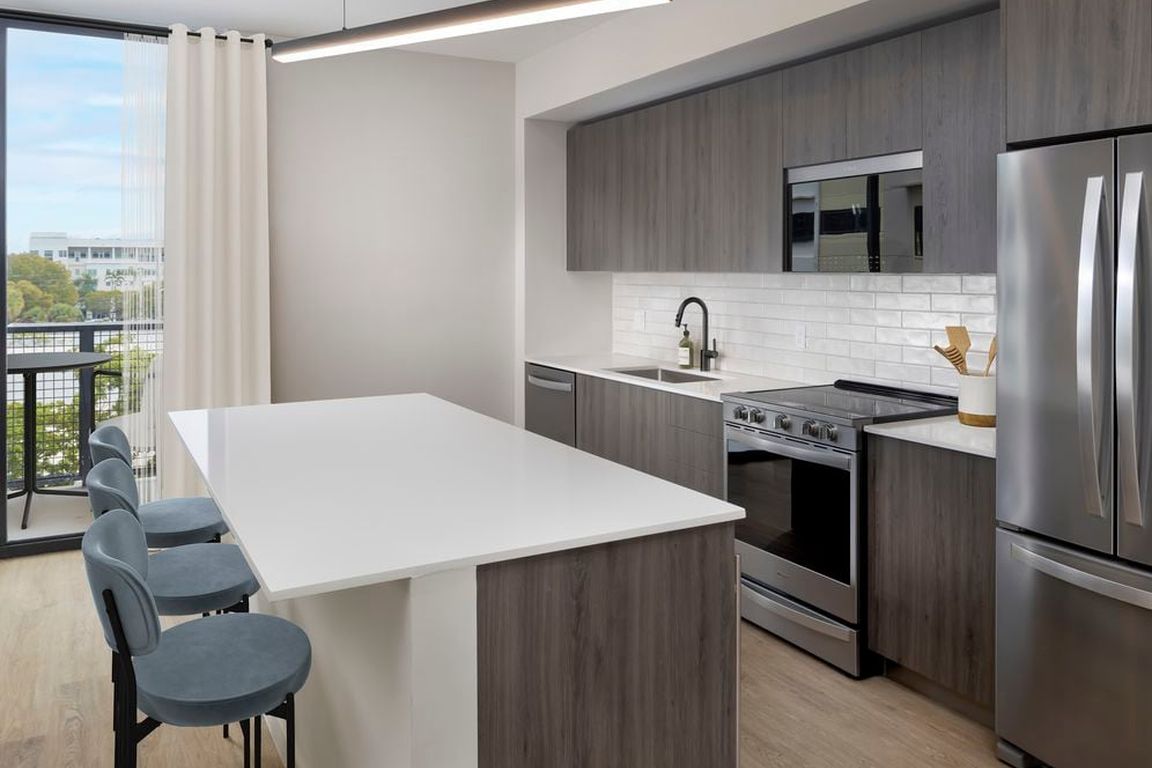 Upgrade Collection II Three-bedroom apartment kitchen with espresso cabinetry, white tile backsplash, white quartz countertop, and hard-surface vinyl plank flooring