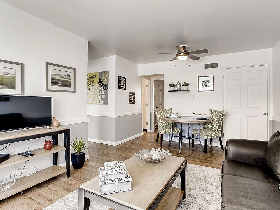 A living room with a black couch a television and a dining table
