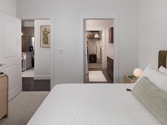 Spacious apartment bedroom with a large closet, attached bathroom, and plush carpet flooring.