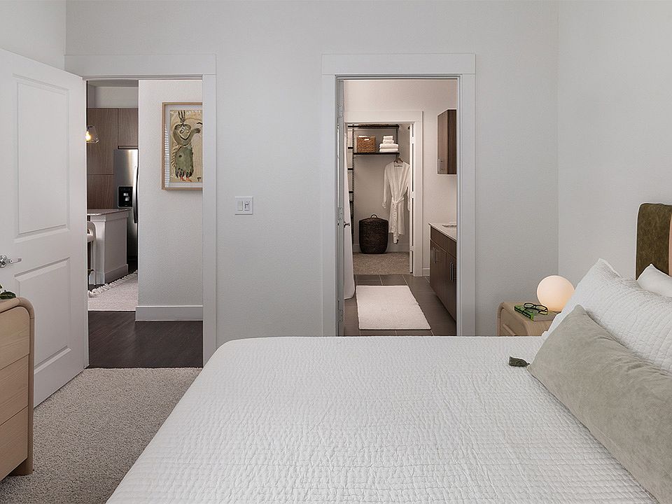 Spacious apartment bedroom with a large closet, attached bathroom, and plush carpet flooring.