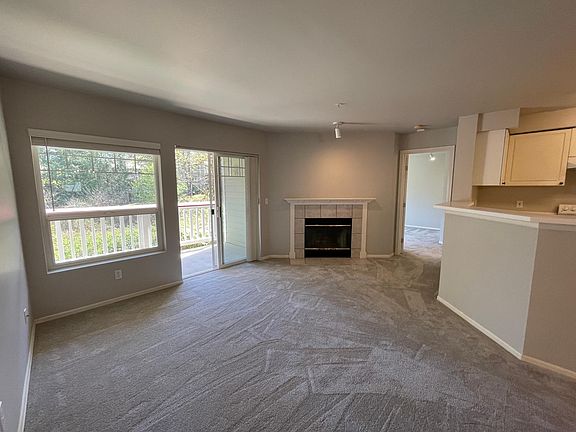 Living room with fireplace and deck overlooking wooded area.