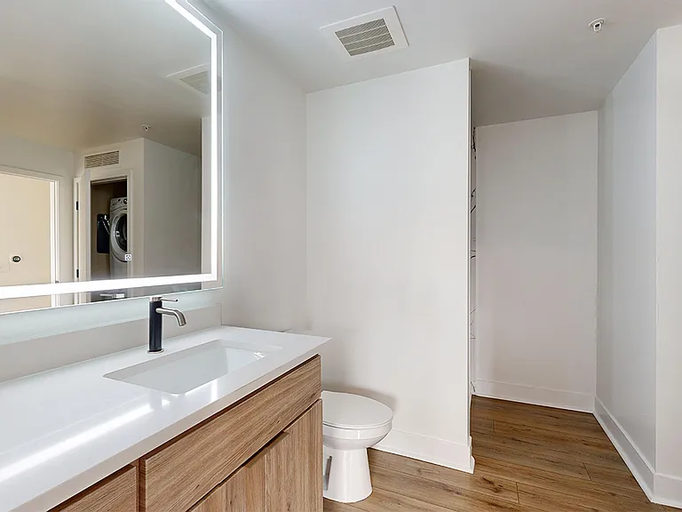 Apartment bathroom with glass-enclosed shower, wood-style flooring, double sinks, and LED vanity mirror.