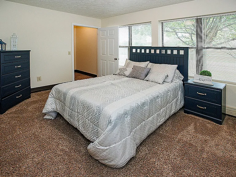 Inviting bedroom with plush carpet, elegant blue furniture, and large windows offering natural light.