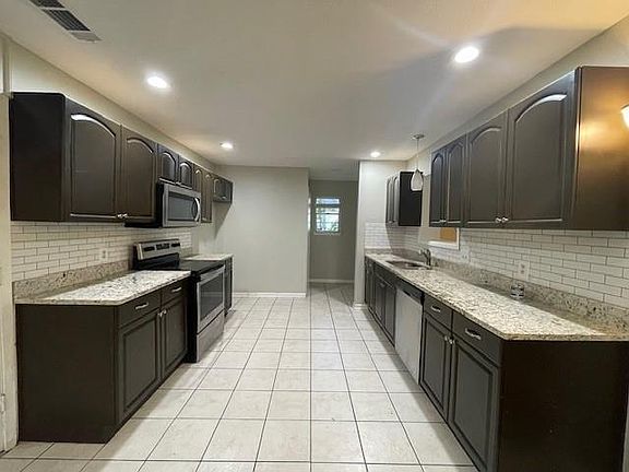 Kitchen with light stone counters, dark brown cabinetry, light tile patterned flooring, sink, and stainless steel appliances