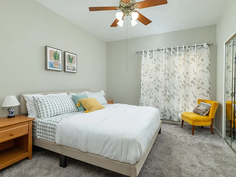 Primary bedroom on the first floor features a king bed, cozy chair, mirrored closet doors, and a ceiling fan for added comfort.